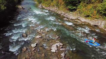 Four sportsmans in blue inflatable canoes are rafting down a mountain river. Aerial view video