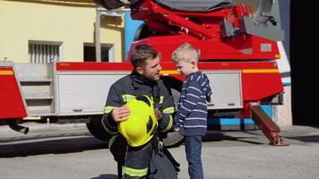 Little boy with firefighter in protective uniform in fire station. Concept of saving lives, fire safety video