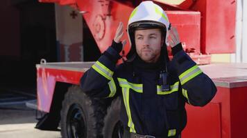 portret van de knap brandweerman in de uitgerust kostuum zet Aan een helm en op zoek naar de camera video