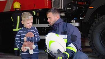 Little boy with firefighter in protective uniform in fire station video