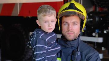 Portrait of firefighter with cute boy on arms. Concept of saving lives, fire safety video