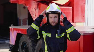 Portrait of the handsome fireman in the equipped costume puts on a helmet and looking to the camera video