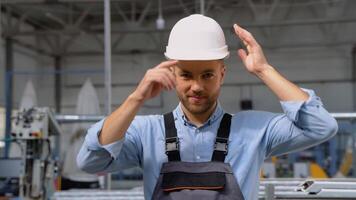 Portrait of the handsome manual man worker in the equipped costume taking off helmet and looking to the camera video