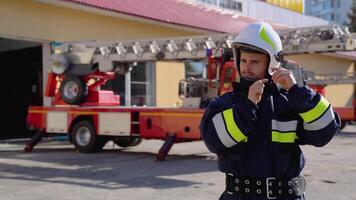 portret van de knap brandweerman in de uitgerust kostuum zet Aan een helm en op zoek naar de camera video