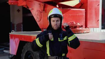 Portrait of the handsome fireman in the equipped costume taking off helmet and looking to the camera video