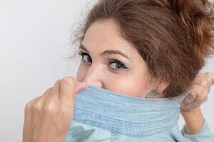Close-up portrait of a young girl covering her face with a denim shirt. photo