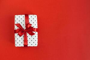 Gift box wrapped in black polka-dot white paper with red bow on red background. photo