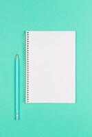 Notebook with blank page and pencil on turquoise background. photo