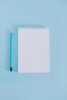cuaderno con blanco página y lápiz en ligero azul antecedentes. foto