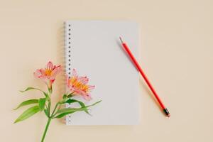 cuaderno con blanco página, rosado flor y lápiz en ligero amarillo antecedentes. foto