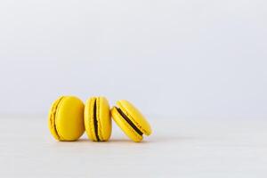 Three yellow french macarons on a wooden table. Banana macarons with chocolate cream. White background. photo