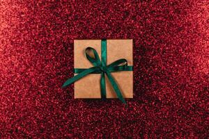 Craft gift box with green bow on dark red sparkle background. Holiday concept. photo
