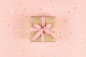 Golden gift box with pink bow on the pink background with golden and silver sparkles. photo