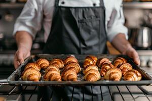 Chef's hands holding baking tray with fresh croissants. photo