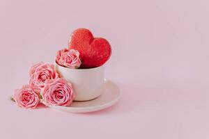 Pink heart shaped french macarons with rose flowers on a pink pastel background. Concept for Valentine's day. photo