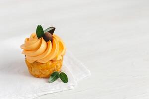 Tasty pumpkin cupcake with orange cream and decoration on white wooden table. photo