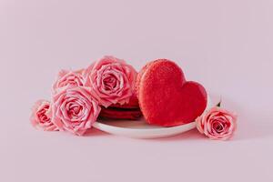 Pink heart shaped french macarons with rose flowers on a pink pastel background. Concept for Valentine's day. Place for text photo