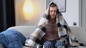 Young man suffering from a common cold and flu or allergy sit at home wrapped in blanket while he have a strong headache pain. Healthcare concept video