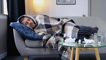 período do sazonal doenças. fechar acima do uma doente homem com gripe, febre e dor de cabeça deitado embrulhado dentro uma xadrez em a sofá. conceito do viral doenças video