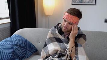doente homem coloca uma comprimir em dele cabeça, dor de cabeça, dor, sentado às casa em a sofá, homem obteve doente video
