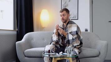 A young man wrapped in a blanket sprays a nasal spray while sitting on sofa video