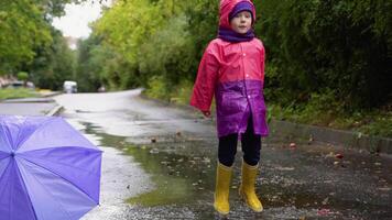 Children with umbrella and rain boots play outdoors in heavy rain. Kid playing out in the rain. Little boy jumping in muddy puddle. Child running in storm video