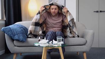 Young man suffering from a common cold and flu or allergy sit at home wrapped in blanket while he have a strong headache pain. Healthcare concept video