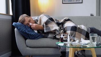 Period of seasonal diseases. Close up of a sick man with flu, fever and headache lying wrapped in a plaid on the couch. A man has runny and common cold. Concept of viral diseases video