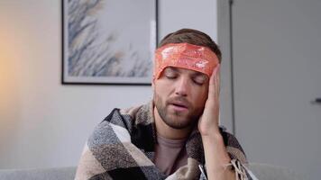 enfermo hombre pone un comprimir en su cabeza, dolor de cabeza, dolor, sentado a hogar en el sofá, hombre tiene enfermo, cerca arriba video