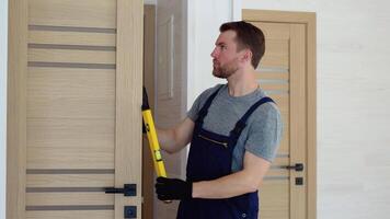 installazione di un' di legno interno porta. ritratto di giovane fabbro ferraio operaio nel uniforme installazione porta. professionale riparazione servizio. Manutenzione concetto video