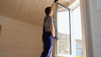 Servicio hombre en uniforme instalando cloruro de polivinilo ventana con medida cinta en de madera prefabricado casa video