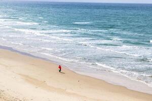 Man walking on the beach on a sunny day with a clear sky and blue ocean waves photo