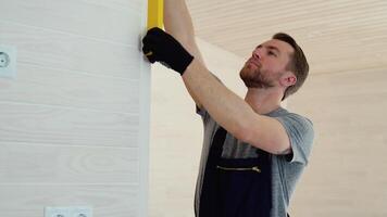 bouwer maatregelen van de verticaal afwijking van de muur in houten modulair huis. bubbel niveau heerser dichtbij omhoog visie, meten en nivelleren concept video