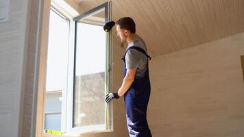 Service man in uniform installing pvc window with measure tape in wooden prefabricated house video