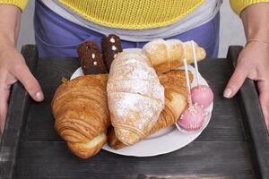 Hands hold a tray with sweets and pastries. photo