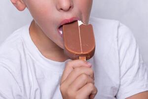 A boy whose face is unrecognizable eats ice cream covered in chocolate. photo