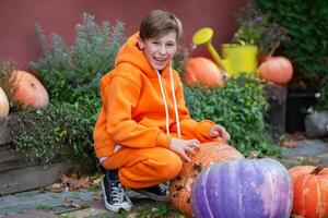 A teenage boy in orange clothes sits near Halloween pumpkins. photo