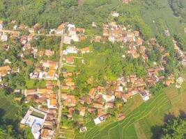 Bird eye view of village among rice fields in Bandung City, Indonesia. Landscape of farmland with rice terrace agricultural crops in countryside. Agricultural Field. Above. Shot from a drone flying photo