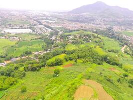 Aerial view of peak Cikancung Hill, Indonesia. Landscape of a green hilltop with plantations. Agricultural Field. Above. Agricultural Industry. Shot from a drone flying 100 meters photo