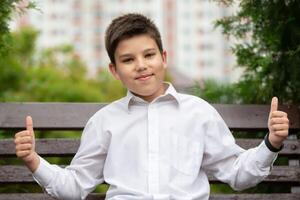 A boy shows a class sign against a background of summer greenery. photo