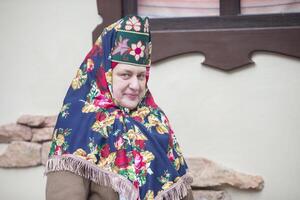 un mayor ruso mujer en un tradicional tocado, kokoshnik, poses en contra el fondo de un pueblo casa. foto