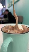 agitare con un' d'oro cucchiaio delizioso caldo cioccolato con marshmallows cosparso con cacao su il sfondo un' uomo nel un' bar berretto menta colore boccale e parete sfondo video