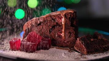 spruzzatina con in polvere zucchero cioccolato folletto buono torta su un' piatto con pezzi di ciliegia gelatina contro il fondale di città luci o Natale albero luci nuovo anni dolce video