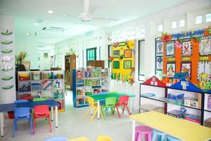 interior de un salón de clases con vistoso mesas y sillas con un pared colgando encima él, un colegio almacenamiento gabinete foto