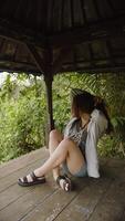 girl sitting in a gazebo against a background of greenery, vertical video