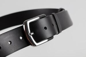 Part of a black leather classic belt with a buckle on a gray background. photo