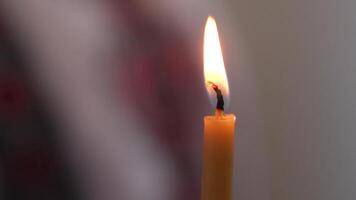 A single white candle burning.Isolated candle burning with dark background. White paraffin candle with yellow shades burns on a black background.Background of remembrance or celebration video