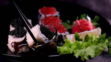 Sushi with red and black caviar Close-up of uramaki sushi rolls with red caviar, salmon, cucumber and avocado isolated on a black background. Delicious traditional Japanese food with sushi rolls. video