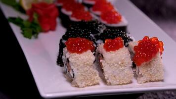 sushi met rood en zwart kaviaar detailopname van uramaki sushi broodjes met rood kaviaar, Zalm, komkommer en avocado geïsoleerd Aan een zwart achtergrond. heerlijk traditioneel Japans voedsel met sushi broodjes. video