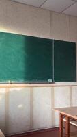 im das Klassenzimmer Dort ist ein Grün Planke, das Schreibtische sind sichtbar, das Licht von das Sonne auf das Tafel. leeren Klassenzimmer mit fliegend Partikel und Sonne Strahlen eintreten von Fenster beim Öffentlichkeit Schule video